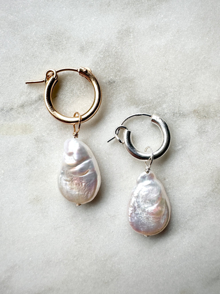 Pair of hoop earrings with teardrop-shaped pearls on a light gray background